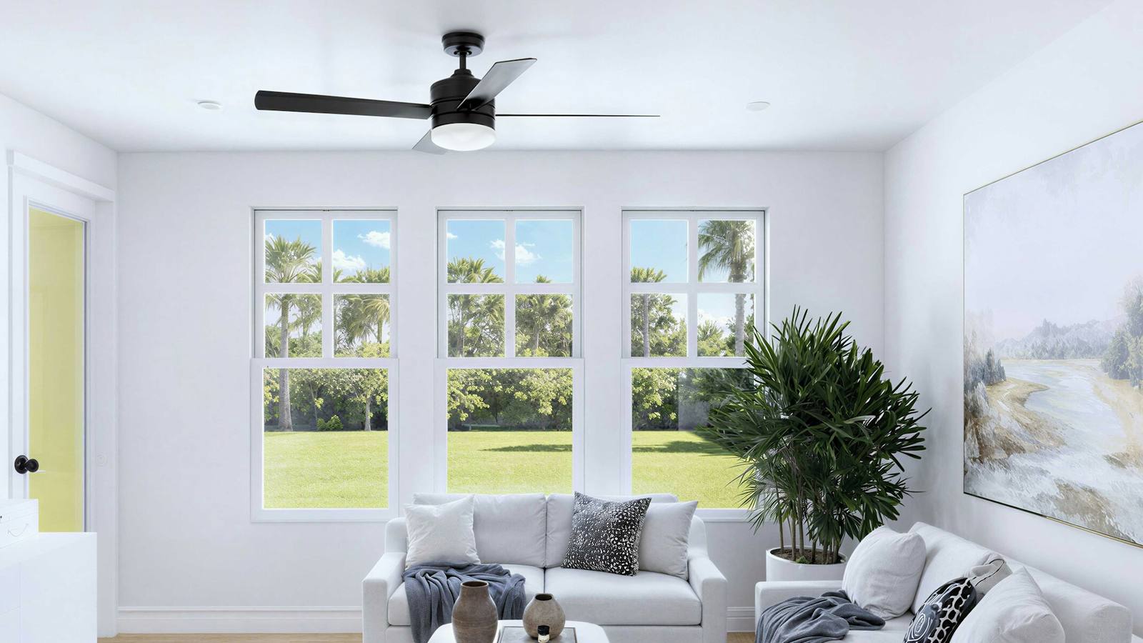 Bright white living room with a ceiling fan and windows looking out to palm trees